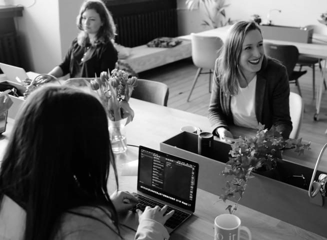 three women in a cafe, two are working and one is laughing at something